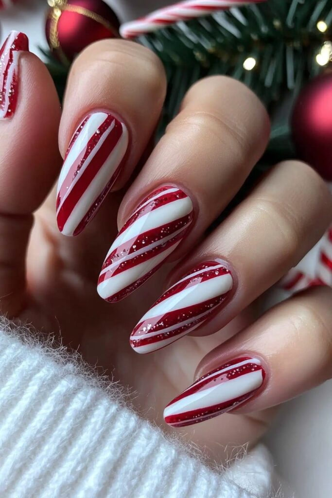 Alt text: "Christmas red acrylic nails with candy cane stripes against holiday decorations