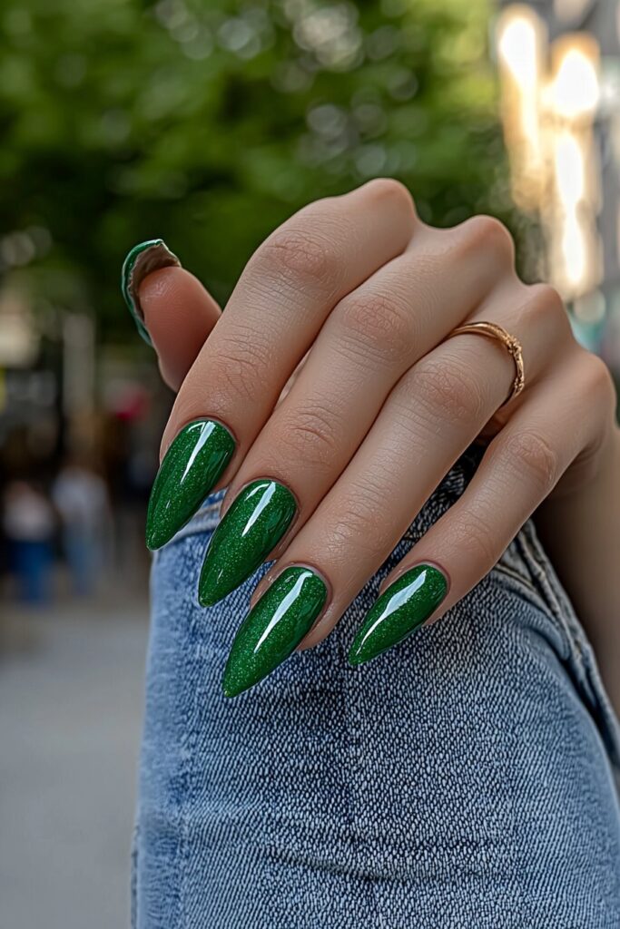 Sparkling emerald green wicked almond nails against denim background