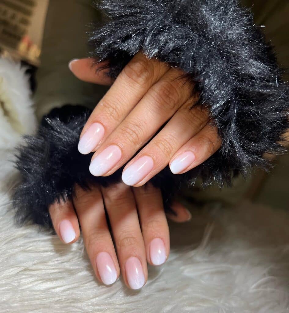 Icy white ombre nails with a glossy finish, styled in a cozy winter setting