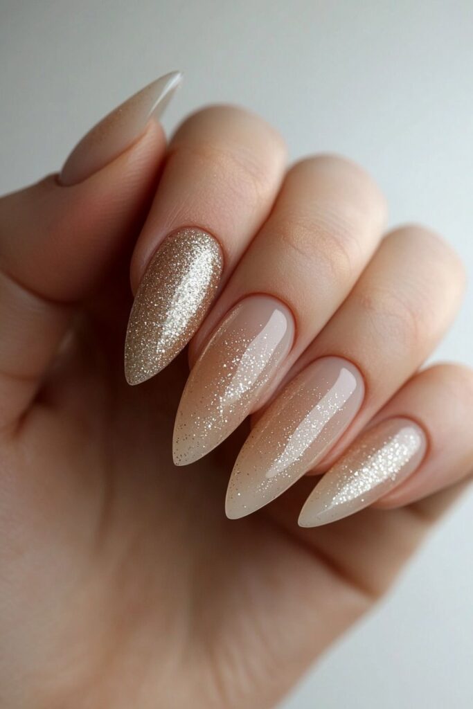 Almond-shaped nails with a glitter ombre effect, fading from a clear base into sparkling gold and silver tips for an elegant touch.