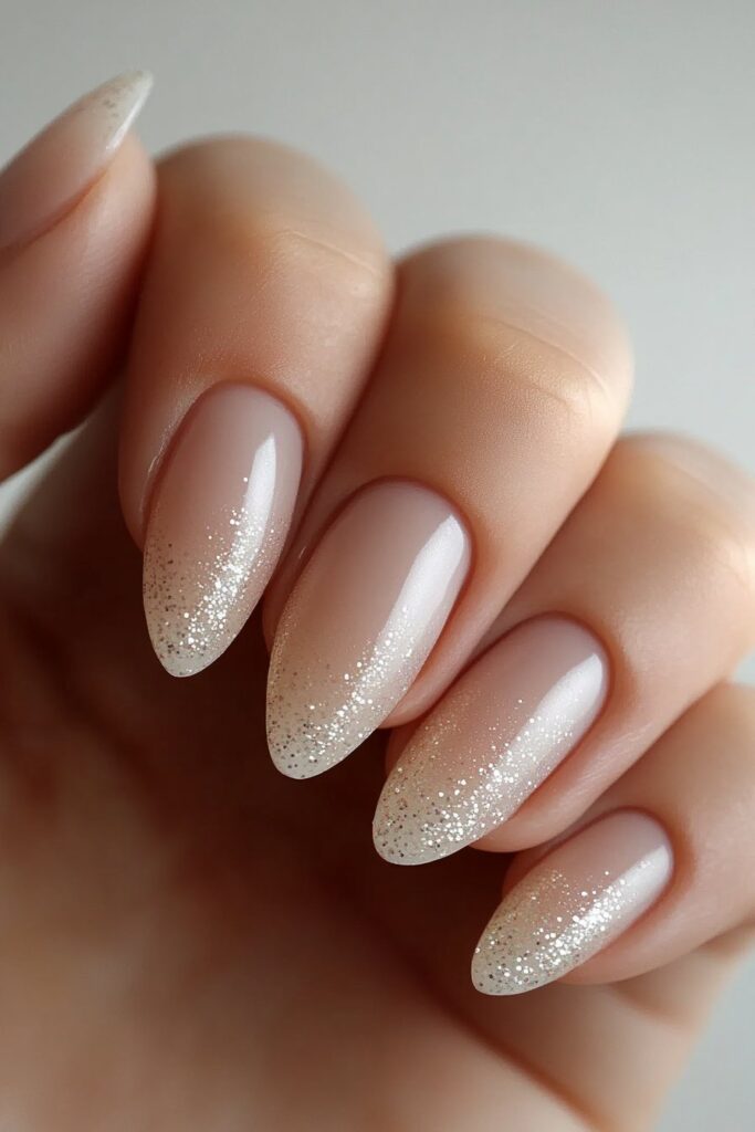 Refined almond-shaped nails with a sheer base and subtle glitter dusted on the tips, creating an elegant shimmer.