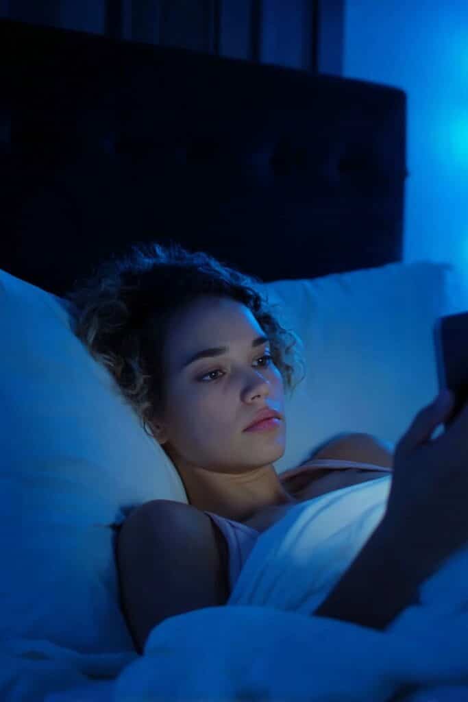 Person putting away electronic devices and using reading light instead, illustrating healthy pre-sleep habits.