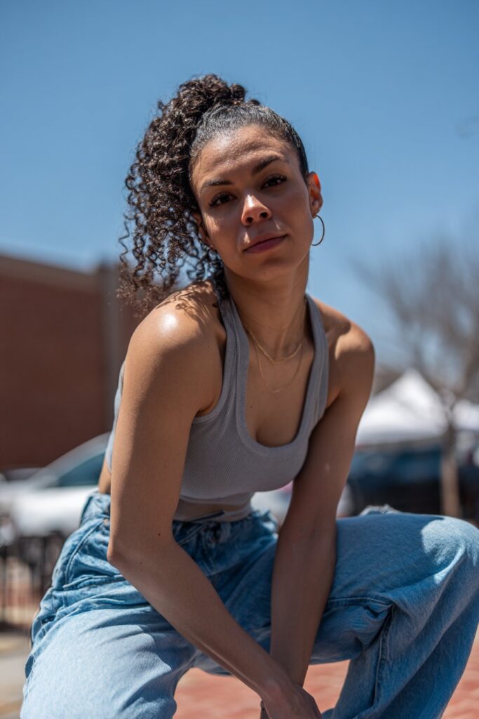 American woman with curly hair in fun bubble ponytail, jazz competition energy, dynamic dance posture, urban brick background.