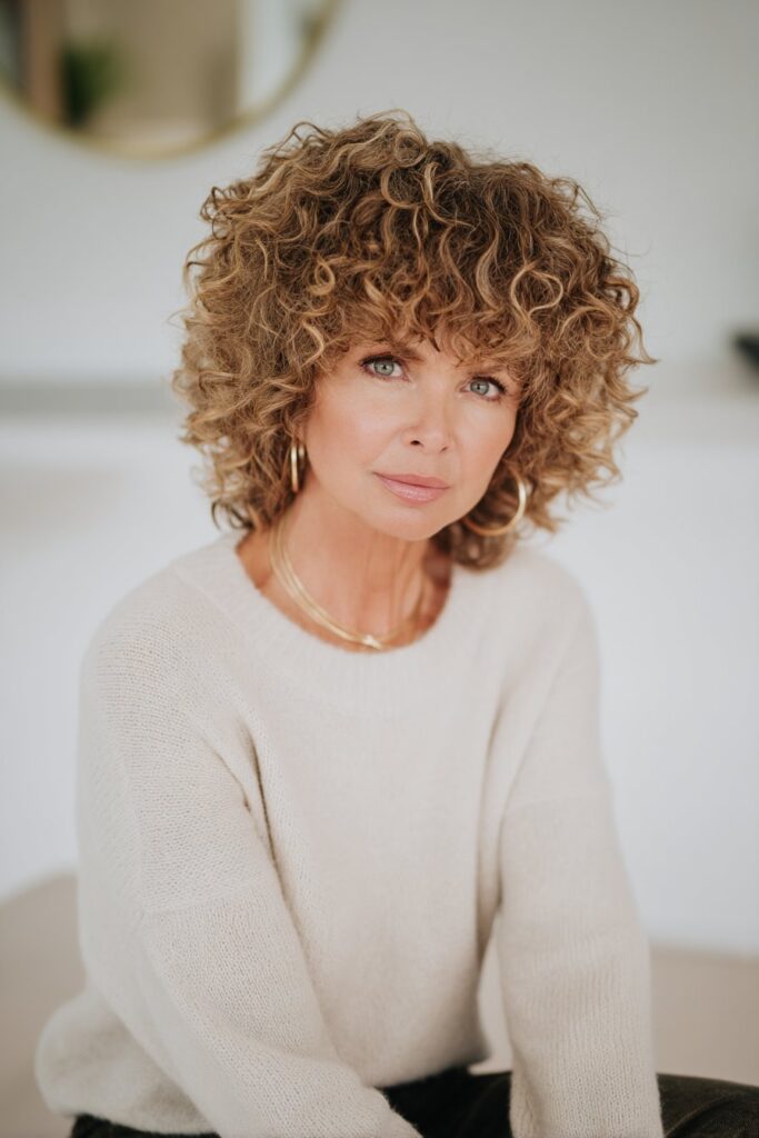 "Professional beauty shot of 50+ woman with thick curly shag and bangs in clean studio setting."