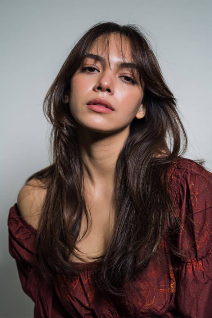 American woman with long layered hair and curtain fringe, sleek styling, trendy outfit photographed against seamless white backdrop.