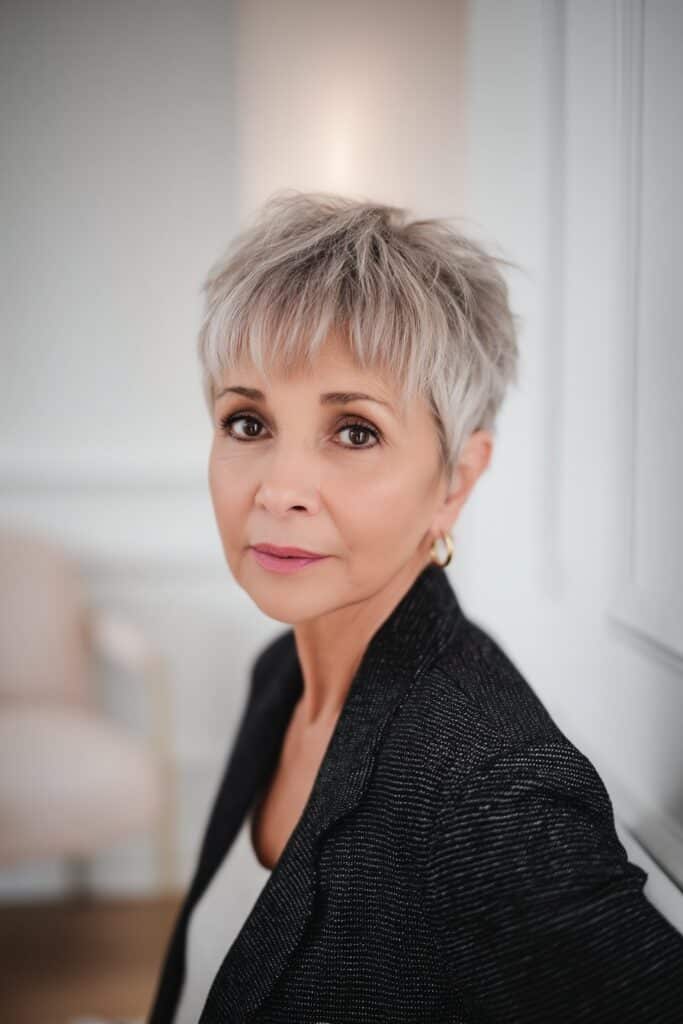 "Professional studio portrait of confident 50+ woman with layered pixie cut against clean white background."