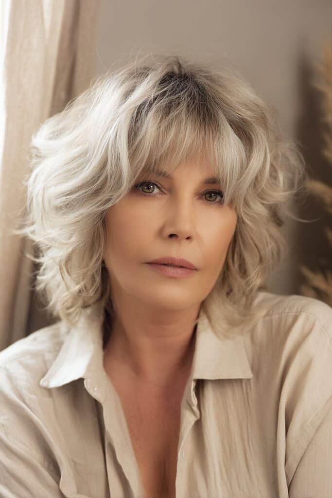 "Sophisticated beauty shot of mature woman with highlighted shaggy bob in soft boho interior setting."