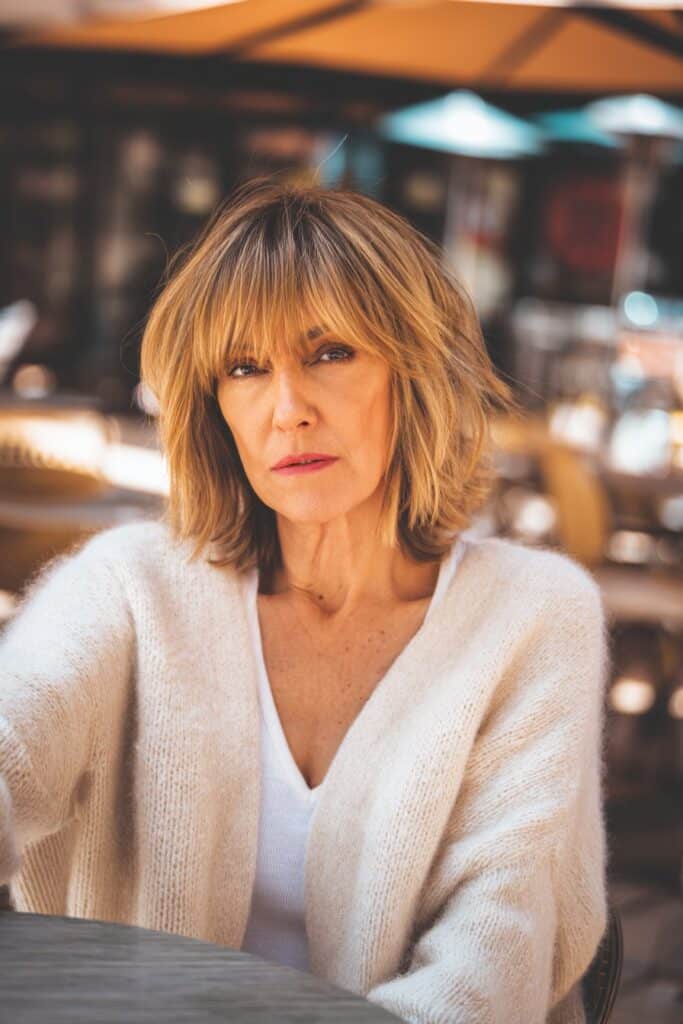 "Warm café portrait of 50+ woman with shaggy lob and curtain bangs in stylish outfit."