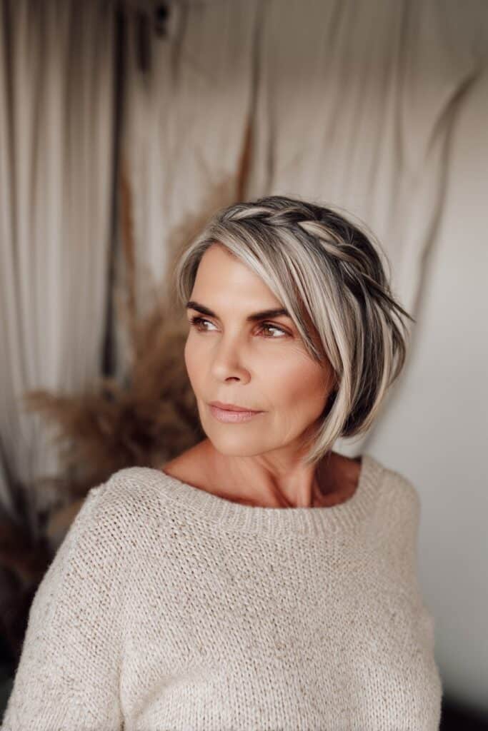 Boho interior portrait of short bob with face-framing layers and braided accents in neutral textured setting.