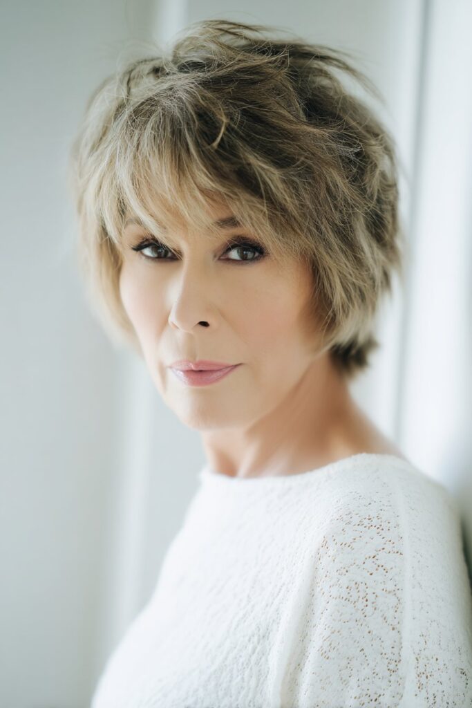 "Clean studio portrait of confident mature woman with short shag hairstyle against minimalist white background."