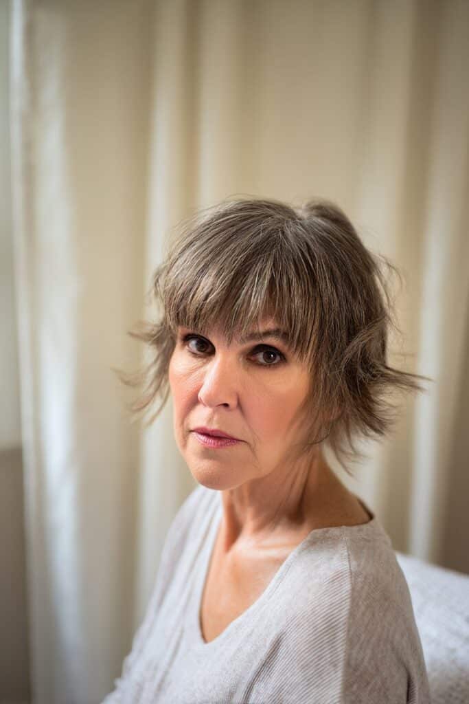 "Elegant portrait of mature woman with curtain-banged short shag in boho indoor setting with neutral textures."