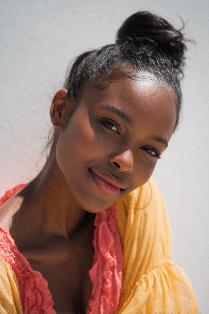 Portrait of a woman with side-parted afro hairstyle against soft gray fabric backdrop, warm expression and natural styling.