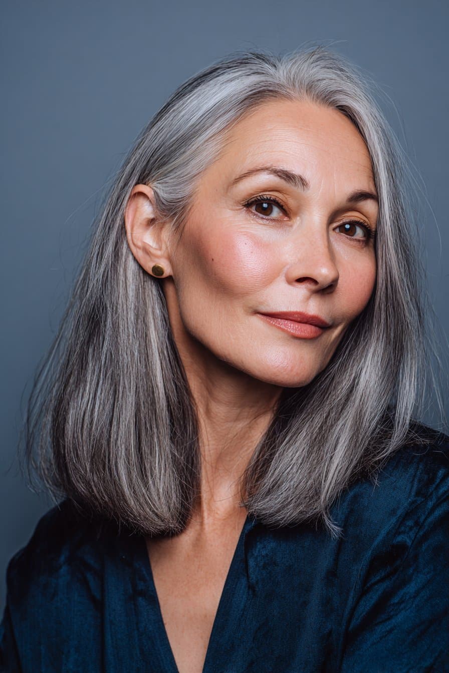 A vibrant female model over 50 with thin fine hair, showcasing a hairstyle for thin fine hair over 50 with a sleek shoulder-length cut, featuring shoulder-length straight cut with sleek finish for shine, captured in a close-up shot focusing on the hair, photographed against a seamless soft navy backdrop with a glossy sheen. She has subtle makeup, an elegant outfit, realistic hair texture, warm skin tone, and a friendly expression, captured with soft natural lighting and an Instagram-style beauty vibe.