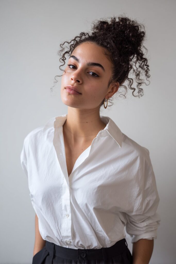 American woman with curly hair in half-up braided hairstyle, stylish competition look, confident stance, white backdrop.