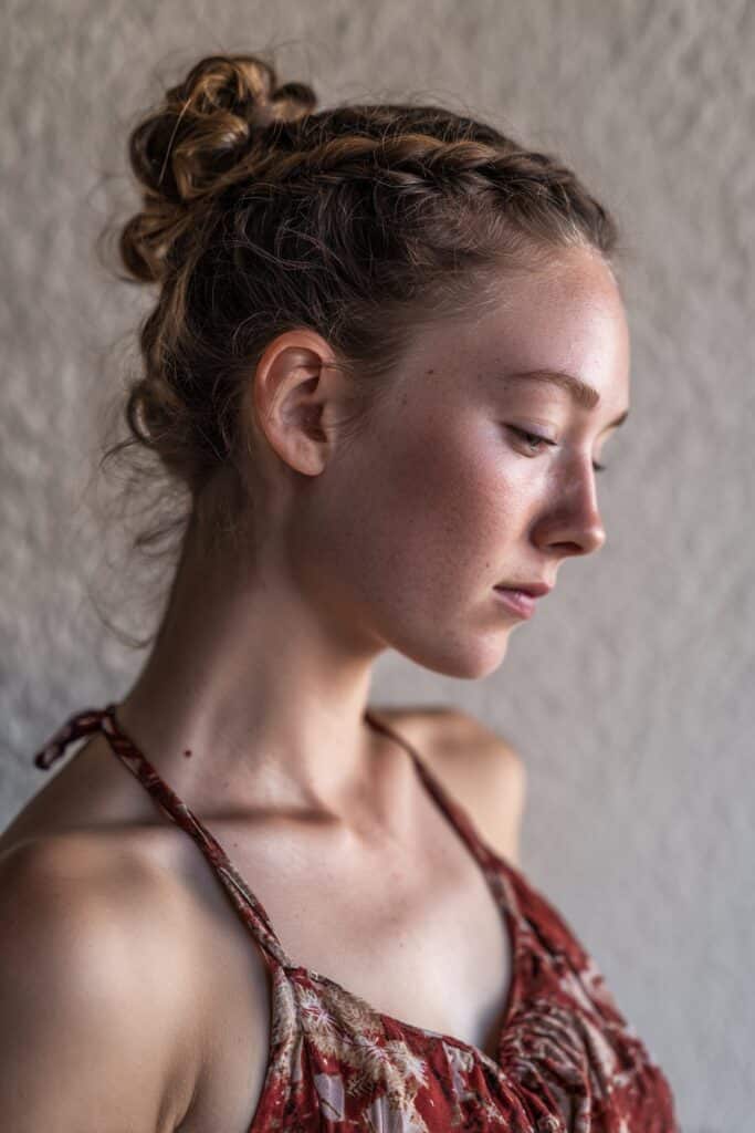 American woman with curly hair in graceful halo braid, contemporary dance costume, flowy attire, textured plaster background.