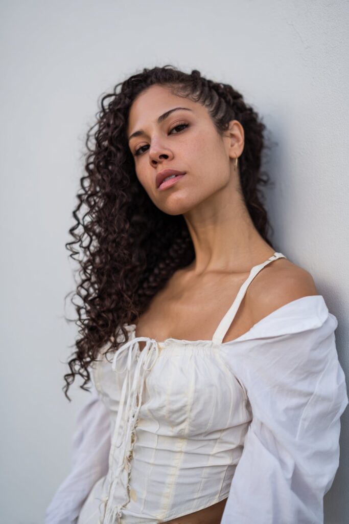 American woman with curly hair in creative snake braid, dramatic dance routine styling, artistic spotlight lighting, white backdrop.