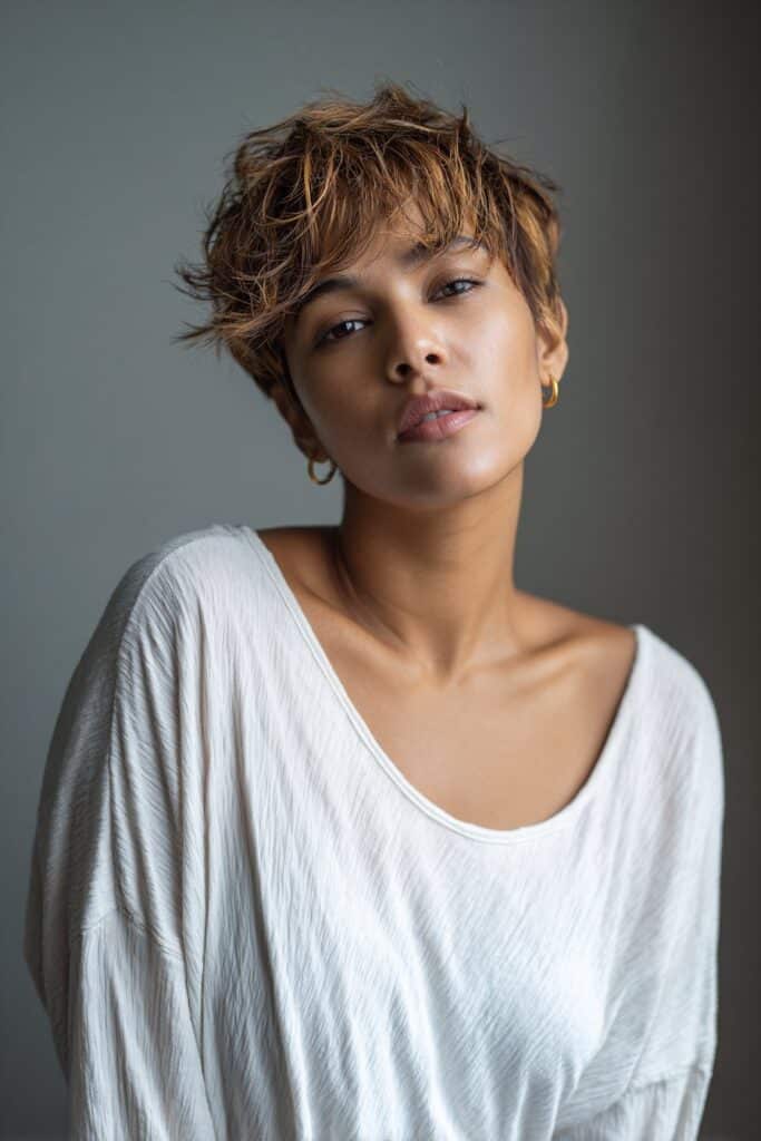 American model with androgynous textured dark pixie cut, soft masculine features, clean outfit, minimal makeup on brick.