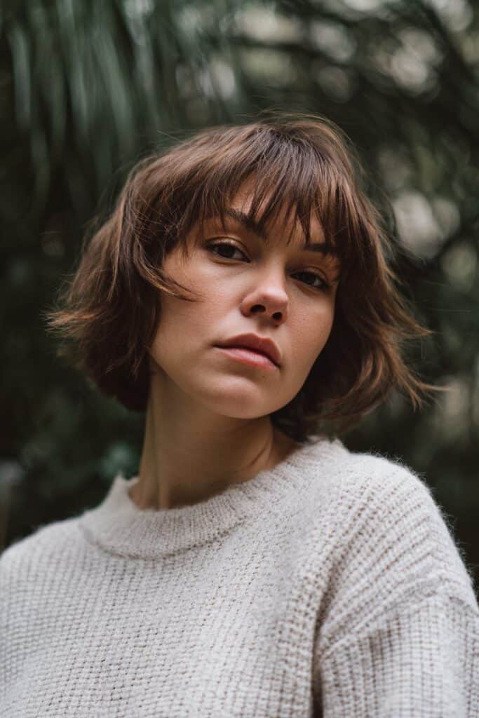 American model with asymmetrical messy pixie cut, side-swept layers, warm brunette tone, light makeup, striped top background.