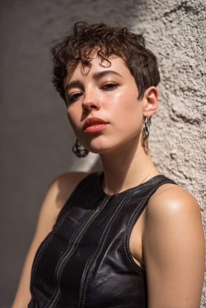 American woman with 4C hair in edgy asymmetrical pixie haircut, bold expression, statement earrings, stylish outfit, textured plaster wall.