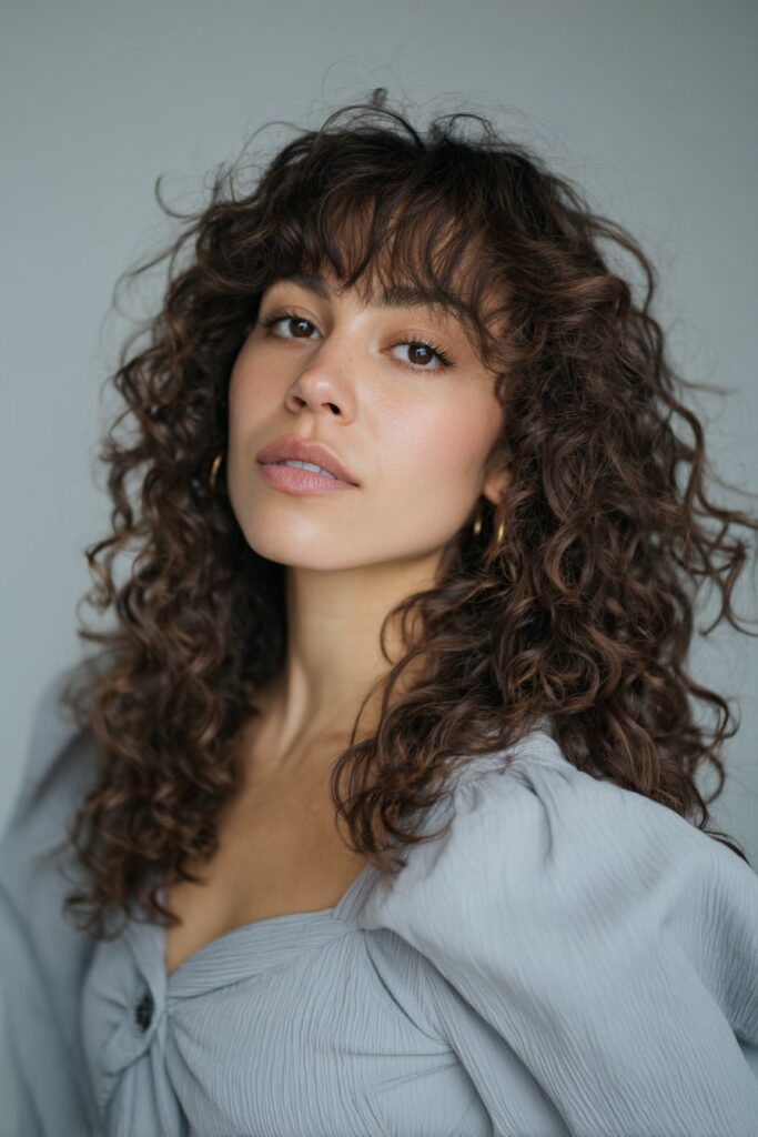 Vintage-style portrait of American woman with Bardot-inspired curtain bangs, retro outfit against soft gray fabric backdrop.
