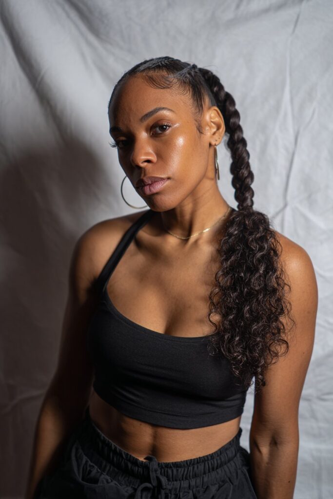 Casual portrait of American woman with sleek braided ponytail ending in soft curls against clean white studio backdrop.