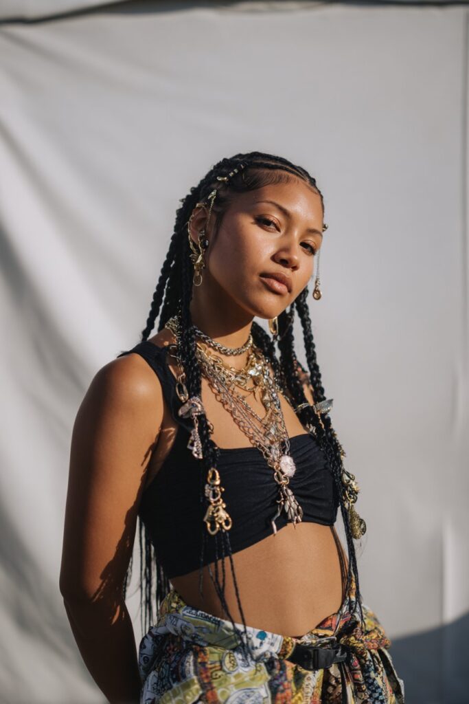 Portrait of American model with long braids decorated with hair cuffs and charms against white studio background.