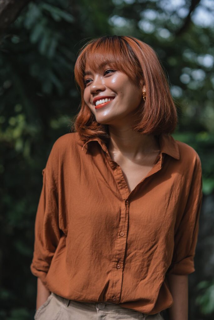 American woman with butterfly haircut, cinnamon brown shade, curtain bangs, feathered layers, natural makeup, forest background.