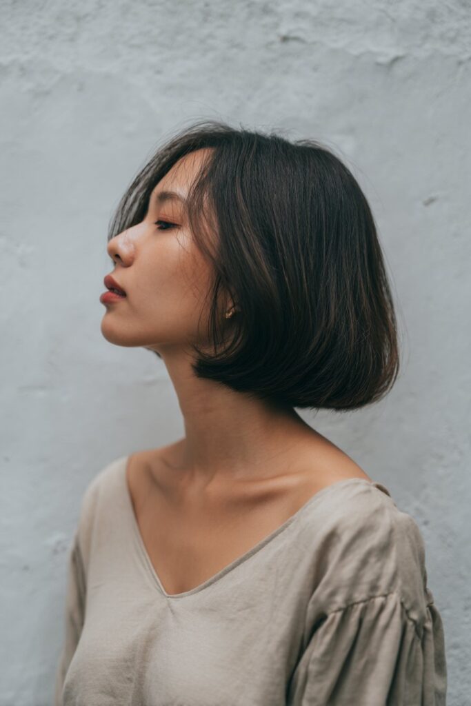 American model with butterfly haircut showing V-shape back, soft feathering, neutral top, side profile, plaster backdrop.