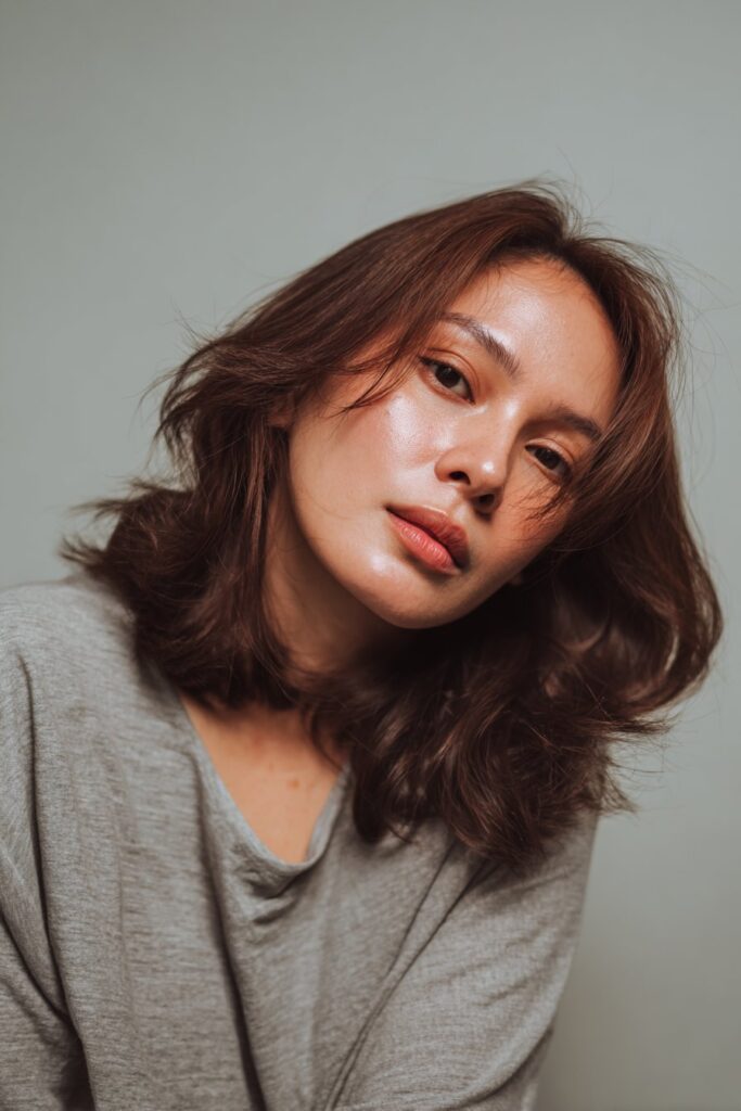 Portrait of American model with round face and fine hair styled in butterfly cut against gray backdrop.