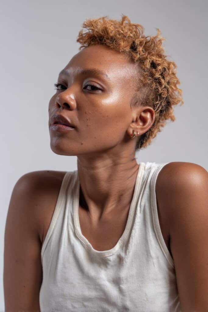 Luminous portrait of Black woman with feathered pixie cut, caramel highlights, airy layered texture against white backdrop.