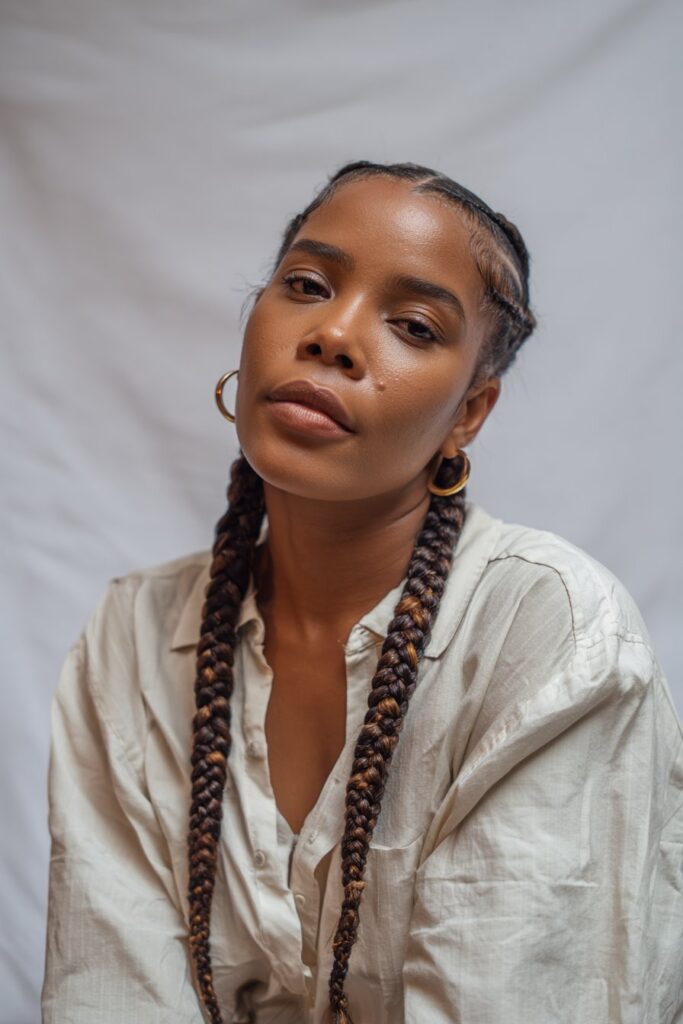 American woman wearing creative freestyle tribal braids with zigzag parting, thick feed-in braids, neutral lip gloss, confident expression.