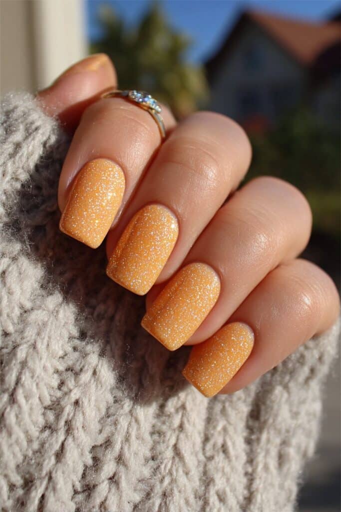 Classic French manicure with vibrant orange tips enhanced by subtle gold accents adding sunny twist to nails.