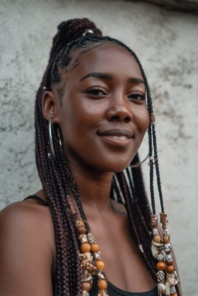 American woman with Fulani tribal braids decorated with wooden and silver beads, long center braid, warm makeup, hoop earrings.