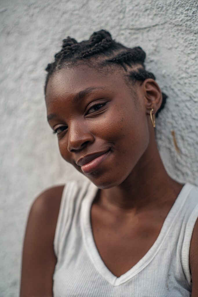 Youthful portrait of Black woman with short 4c hair half up half down, defined texture against plaster backdrop.