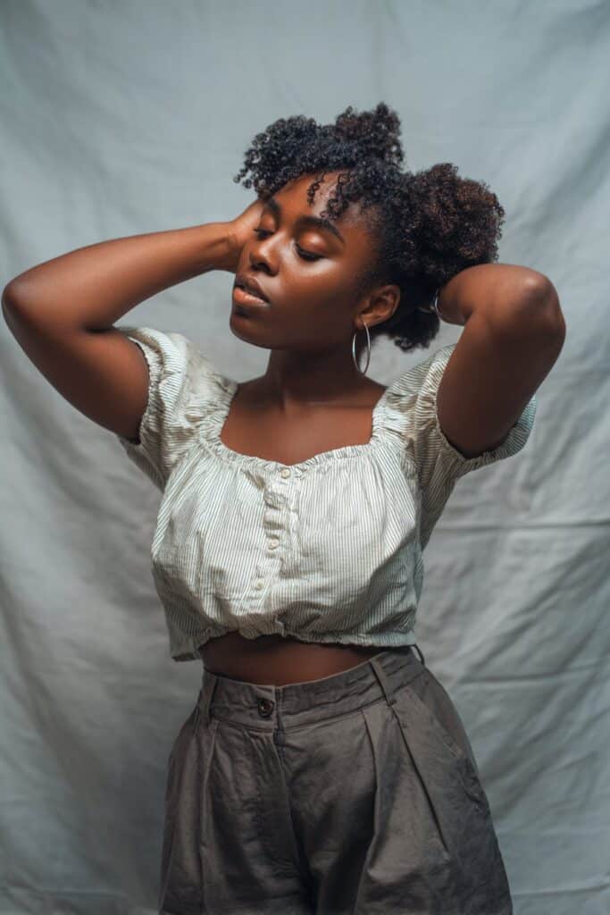 Fun portrait of Black woman with short 4c hair in half-up space buns, loose curls against gray backdrop.