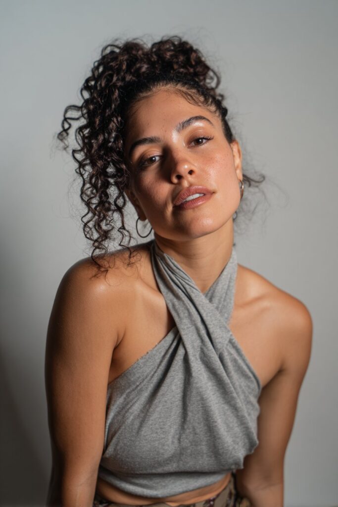 Studio portrait of American model with mid-back knotless braids featuring soft curly ends against soft gray fabric backdrop.