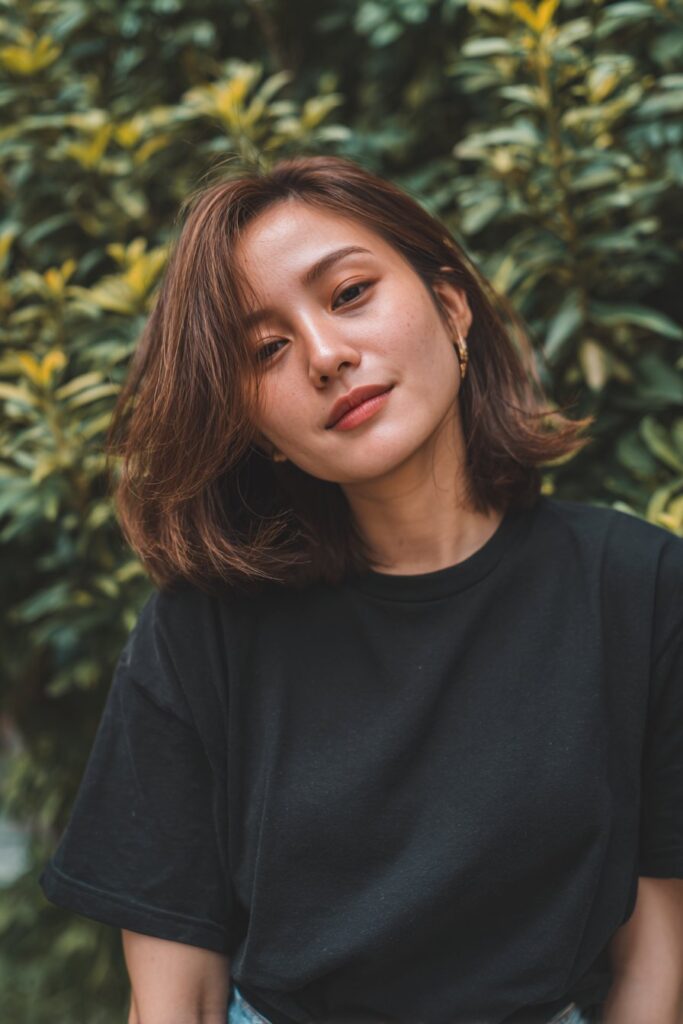 Natural portrait of American female model with round face and medium-length butterfly haircut in forest setting.
