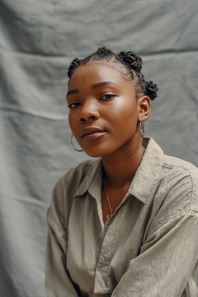 Protective portrait of Black American woman with short 4c hair in neat mini twists, casual look against gray backdrop.