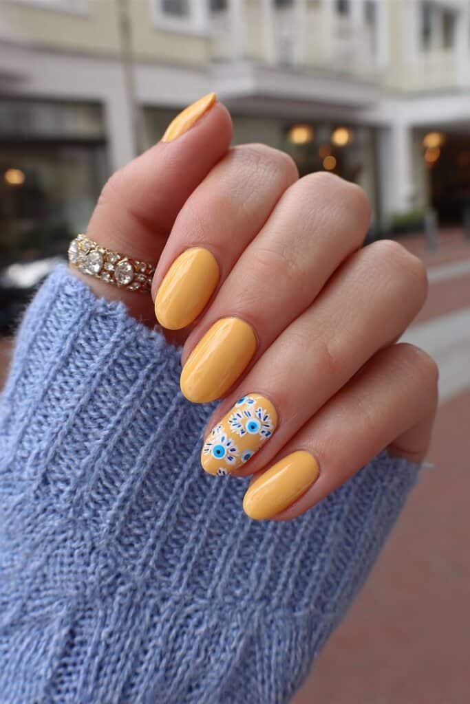 Bold orange summer nails featuring tiny blue and white evil eye accents on few fingers creating playful.