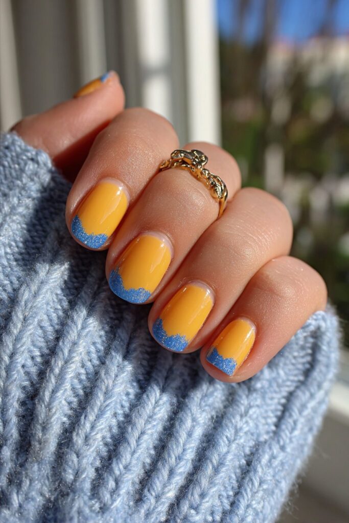 Summer nails with orange bases and deep blue crescent shapes at cuticle creating bold color contrast design.