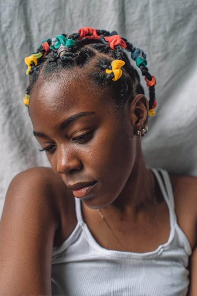 Trendy portrait of Black American woman with short 4c hair in colorful rubber band criss-cross pattern against gray backdrop.
