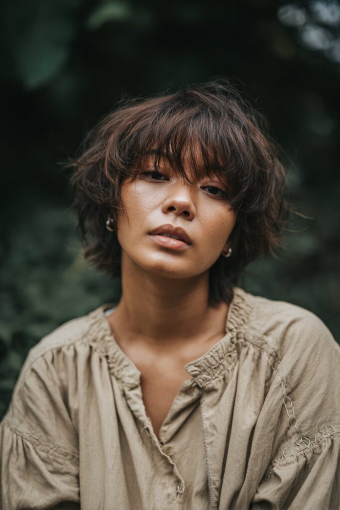 Casual portrait of Black American woman with shaggy layered pixie cut, tousled voluminous texture in natural forest setting.