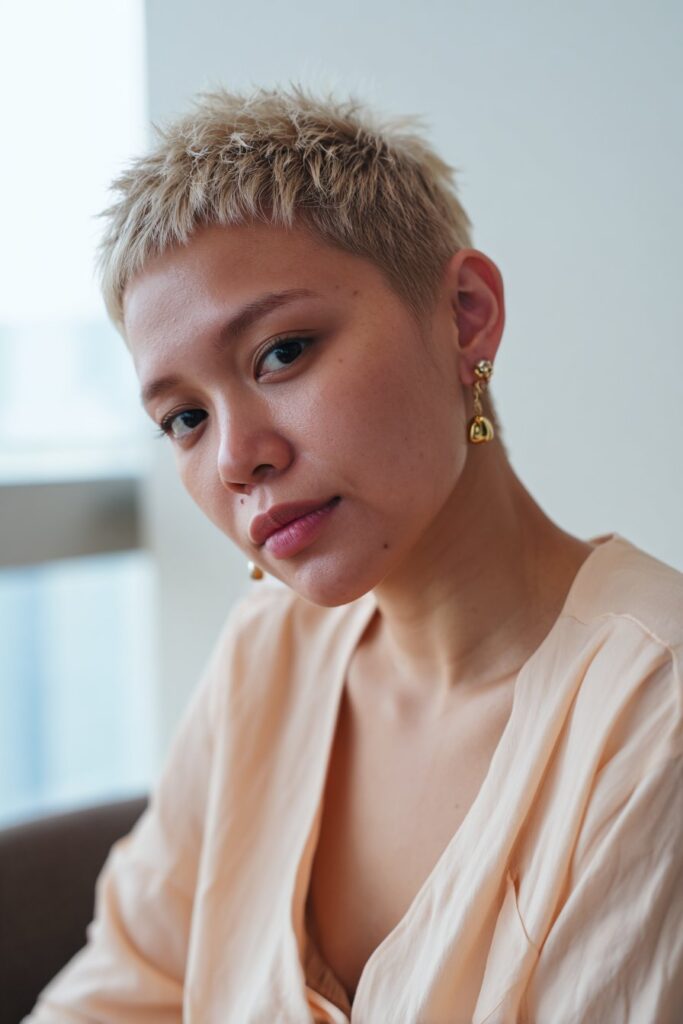American woman with delicate features and soft short spiky pixie cut wearing pastel outfit against white background.