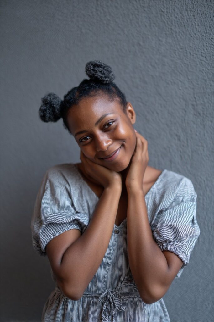 Cheerful portrait of Black American woman with short 4c hair in playful space buns against soft gray backdrop.