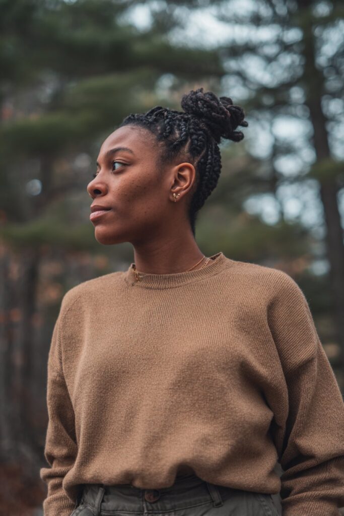 Edgy portrait of American woman with small tight braids in high ponytail inspired by Spice Girls against forest.