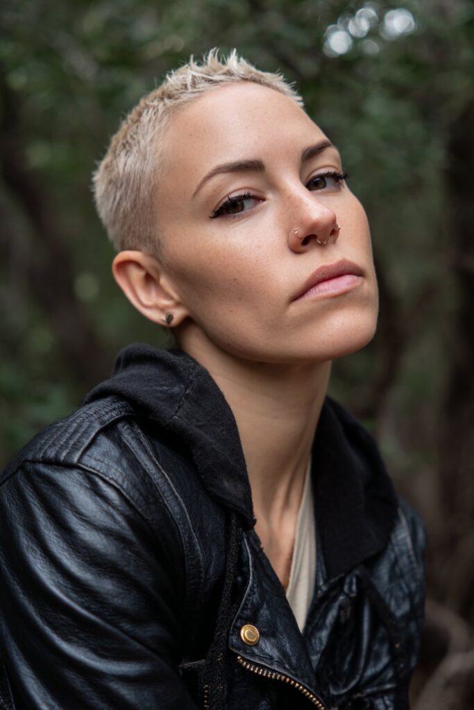 Bold American model with spiky faux hawk and shaved sides wearing urban streetwear against natural forest backdrop.
