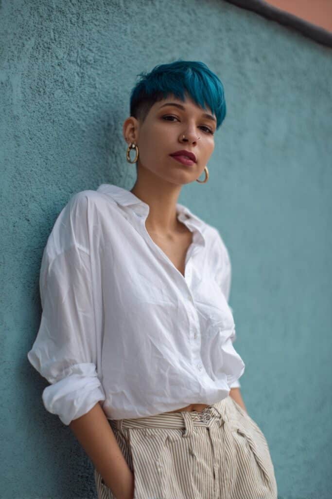 Bold portrait of American woman with vividly colored stacked pixie haircut, confident pose against plaster wall.