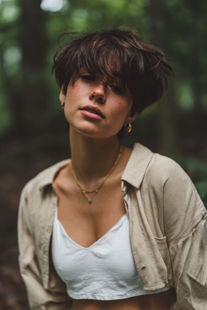 Relaxed portrait of American woman with tousled stacked pixie, voluminous top layers in natural forest setting.