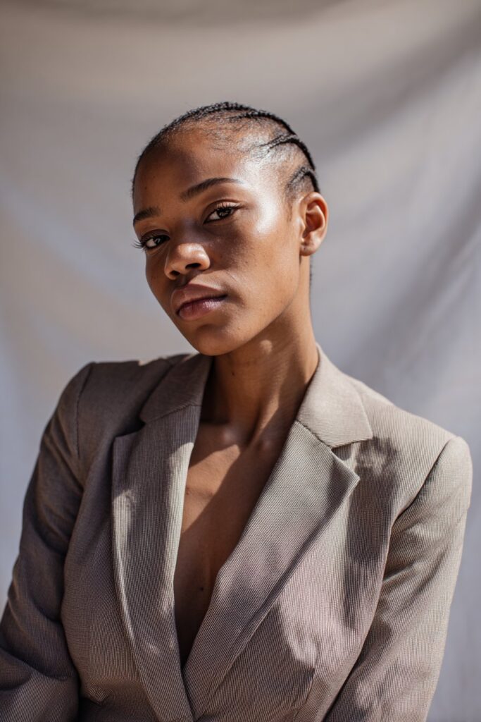 Black woman with very low cut, subtle part line detail, clean sharp style, fitted blazer, seamless white backdrop.