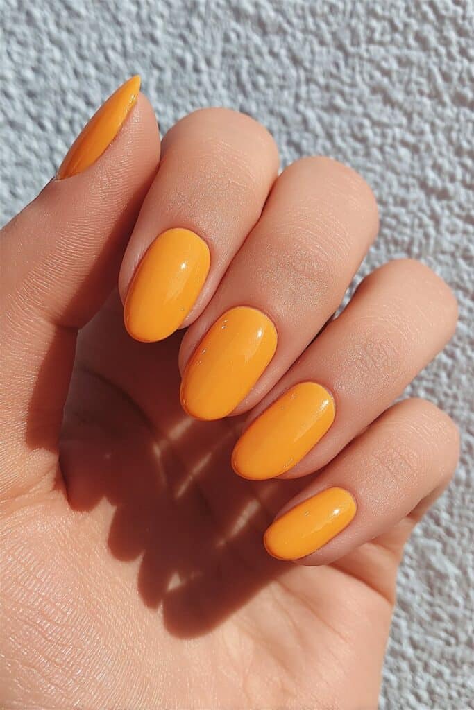 Long summer nails painted in iconic Hermès bright orange shade creating bold fashion-forward glossy finish manicure.